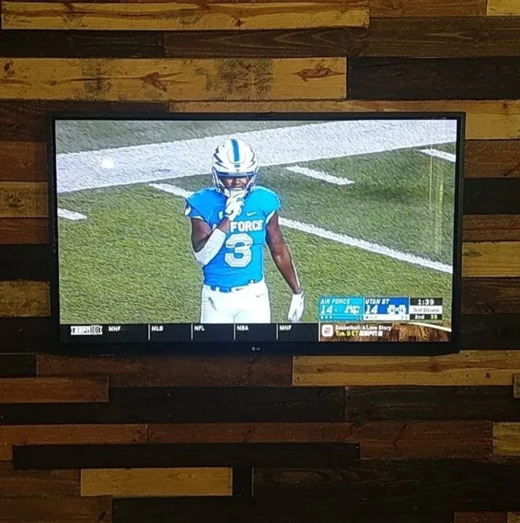 Television, playing a football game, mounted on a modern wooden wall