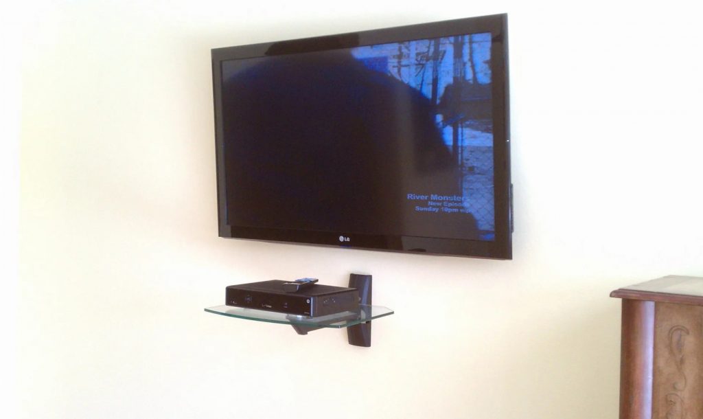 Television mounted on wall, with a small shelf for a cable box mounted underneath